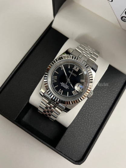 Datejust (Black Roman) Seiko NH35 automatic mod watch. A black dial watch with a silver fluted bezel and jubilee bracelet inside a box in a high angle shot.