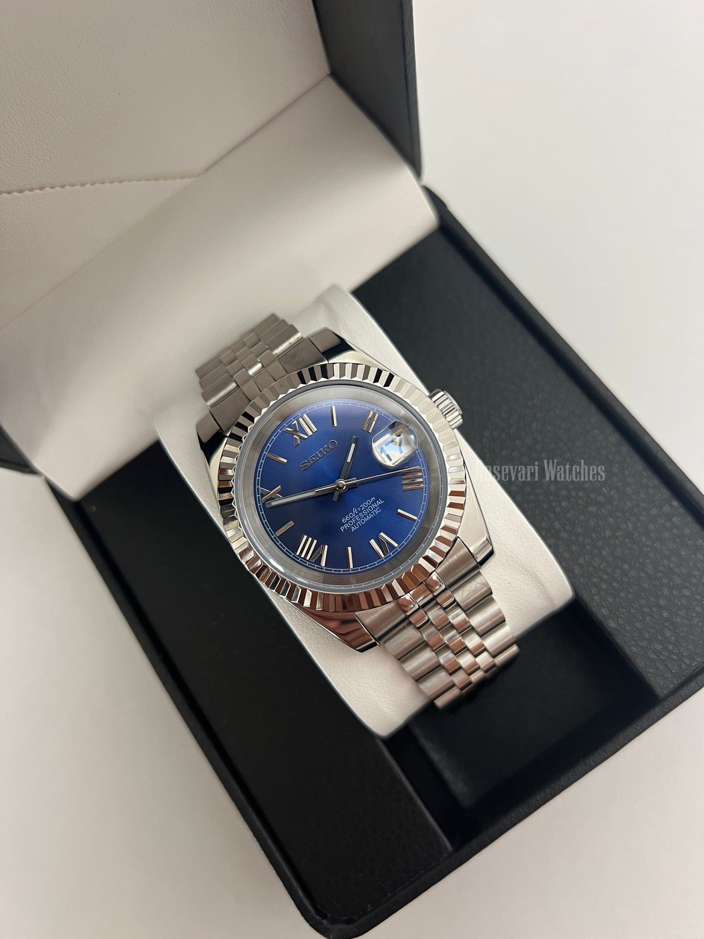 Datejust (Royal Blue Roman) Seiko NH35 automatic mod watch. A blue dial watch with a silver fluted bezel and jubilee bracelet shown in a box from a high angle.