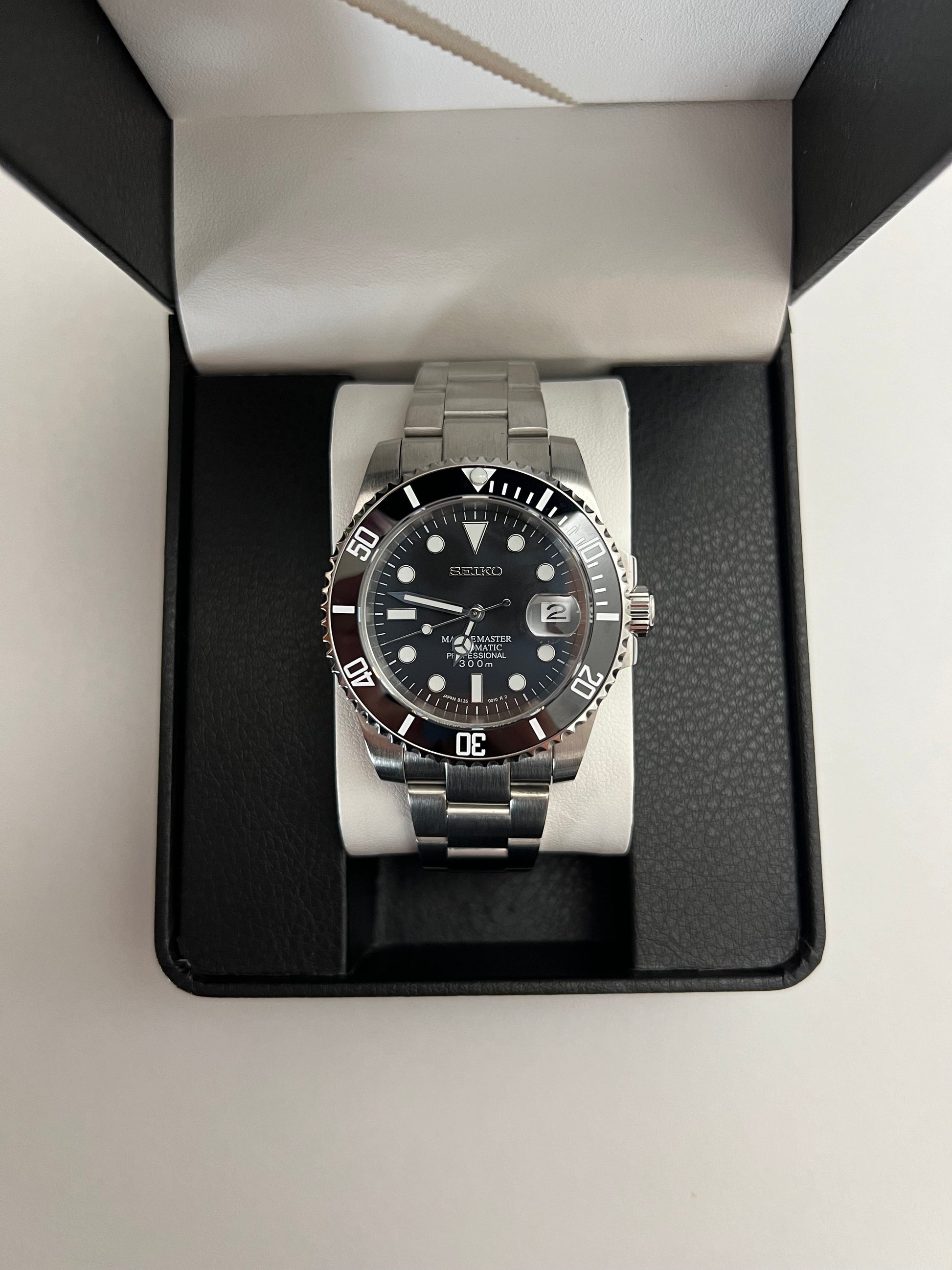 Submariner (Black) Seiko NH35 automatic mod watch. A full watch with a black dial and black bezel on a metal bracelet inside an open black box.