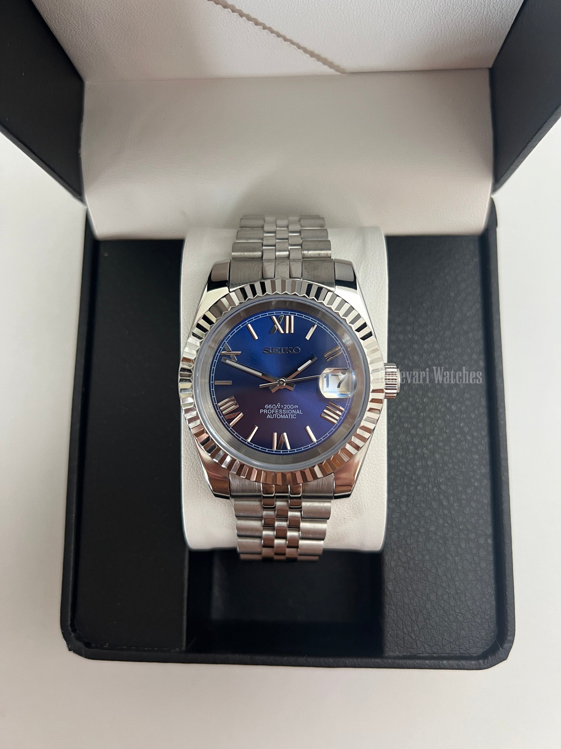 Datejust (Royal Blue Roman) Seiko NH35 automatic mod watch. A blue dial watch with a silver fluted bezel and jubilee bracelet shown in a box from a front view.