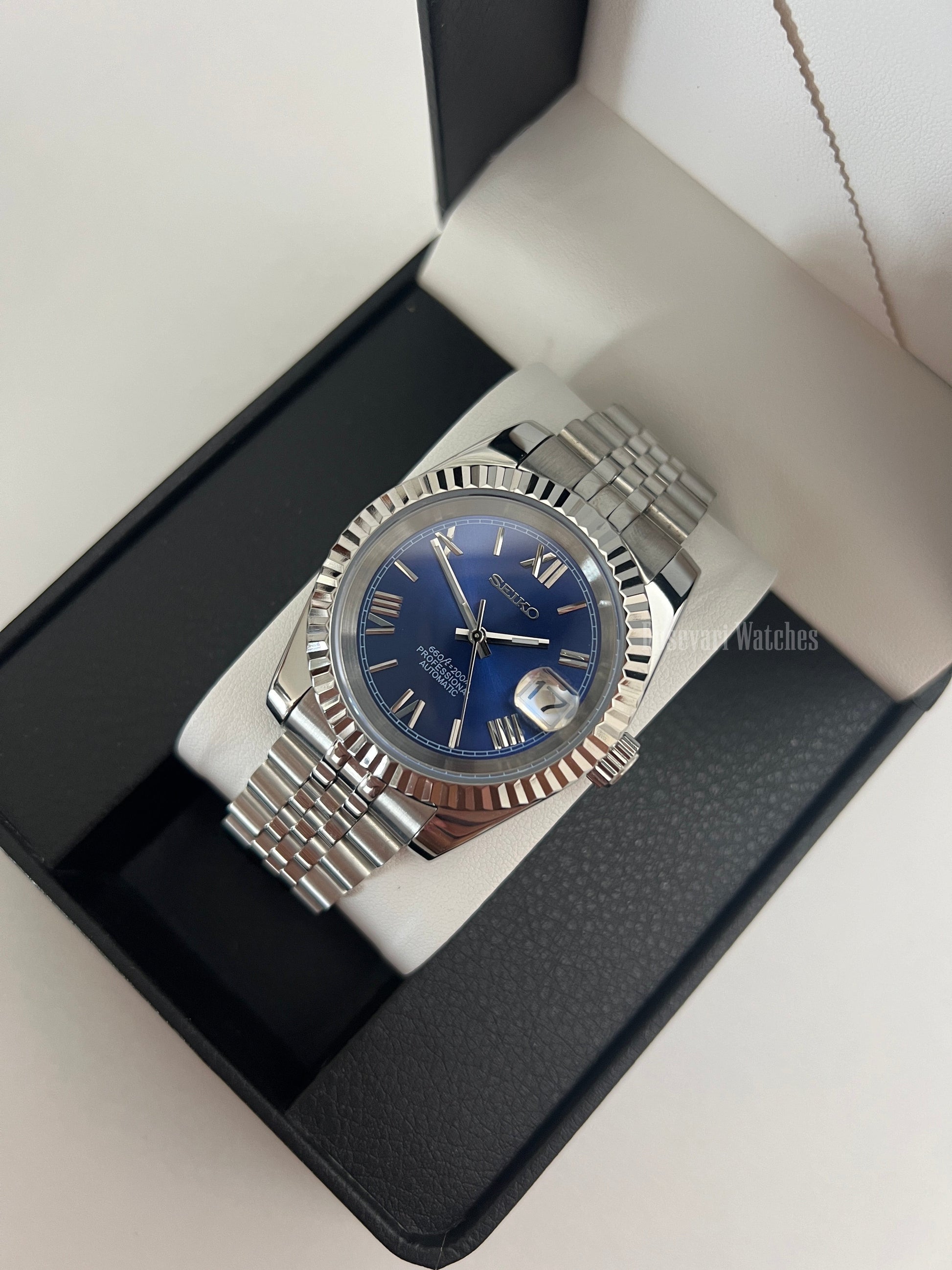 Datejust (Royal Blue Roman) Seiko NH35 automatic mod watch. A blue dial watch with a silver fluted bezel and jubilee bracelet shown in a box from a high angle.