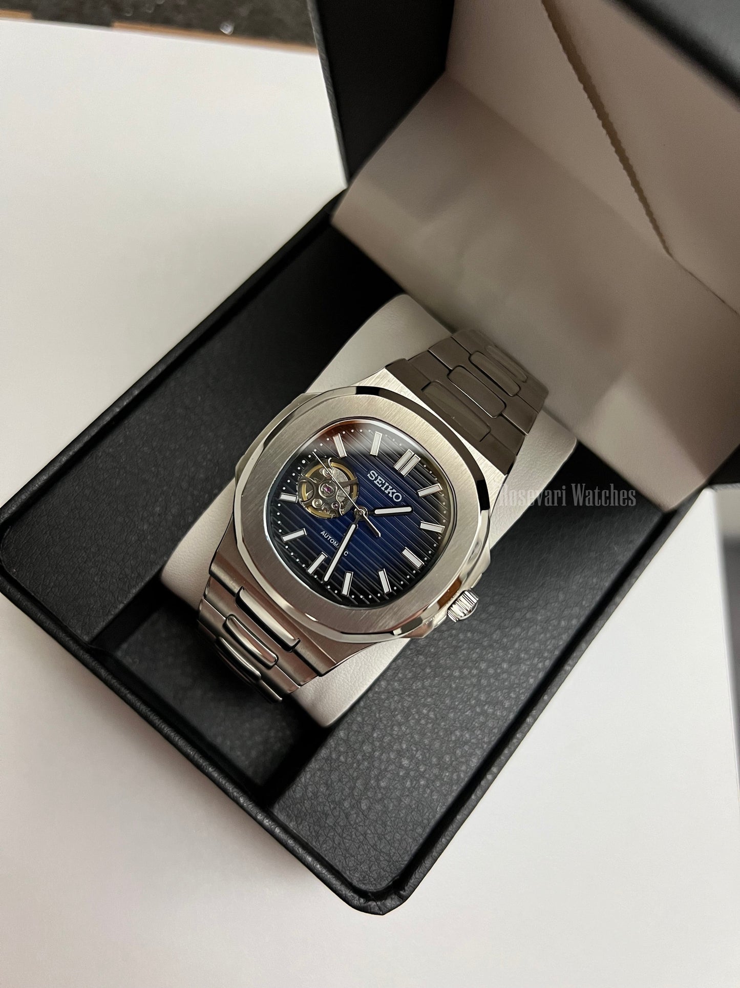 Nautilus (Open Heart, Royal Blue) Seiko NH38 open-heart automatic mod watch. A full watch shot in a box showing a blue dial and silver bezel with a metal link bracelet.