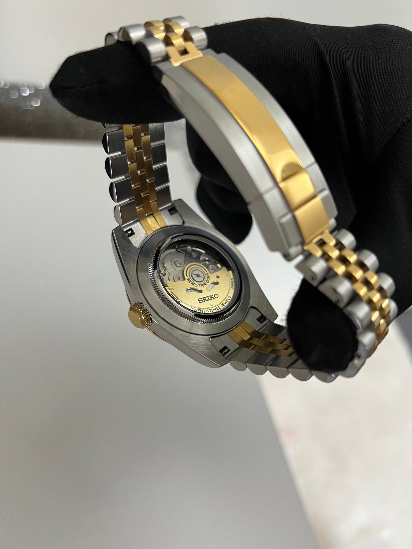 Datejust (Two-Tone White Roman) Seiko NH35 automatic mod watch. A gloved hand holds the watch to show the clear caseback revealing the internal movement and gold rotor.