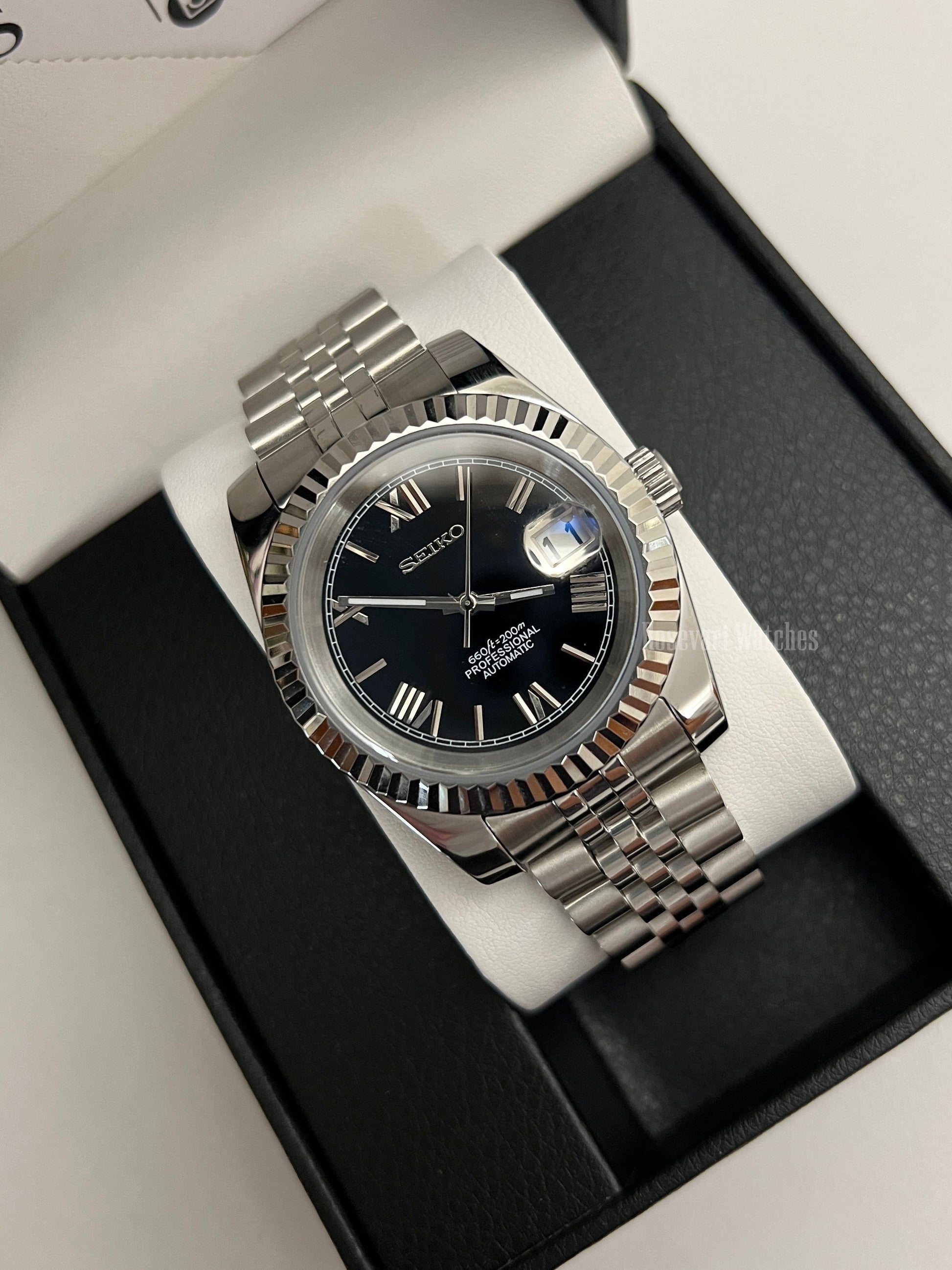 Datejust (Black Roman) Seiko NH35 automatic mod watch. A black dial watch with a silver fluted bezel and jubilee bracelet inside a box in a high angle shot.