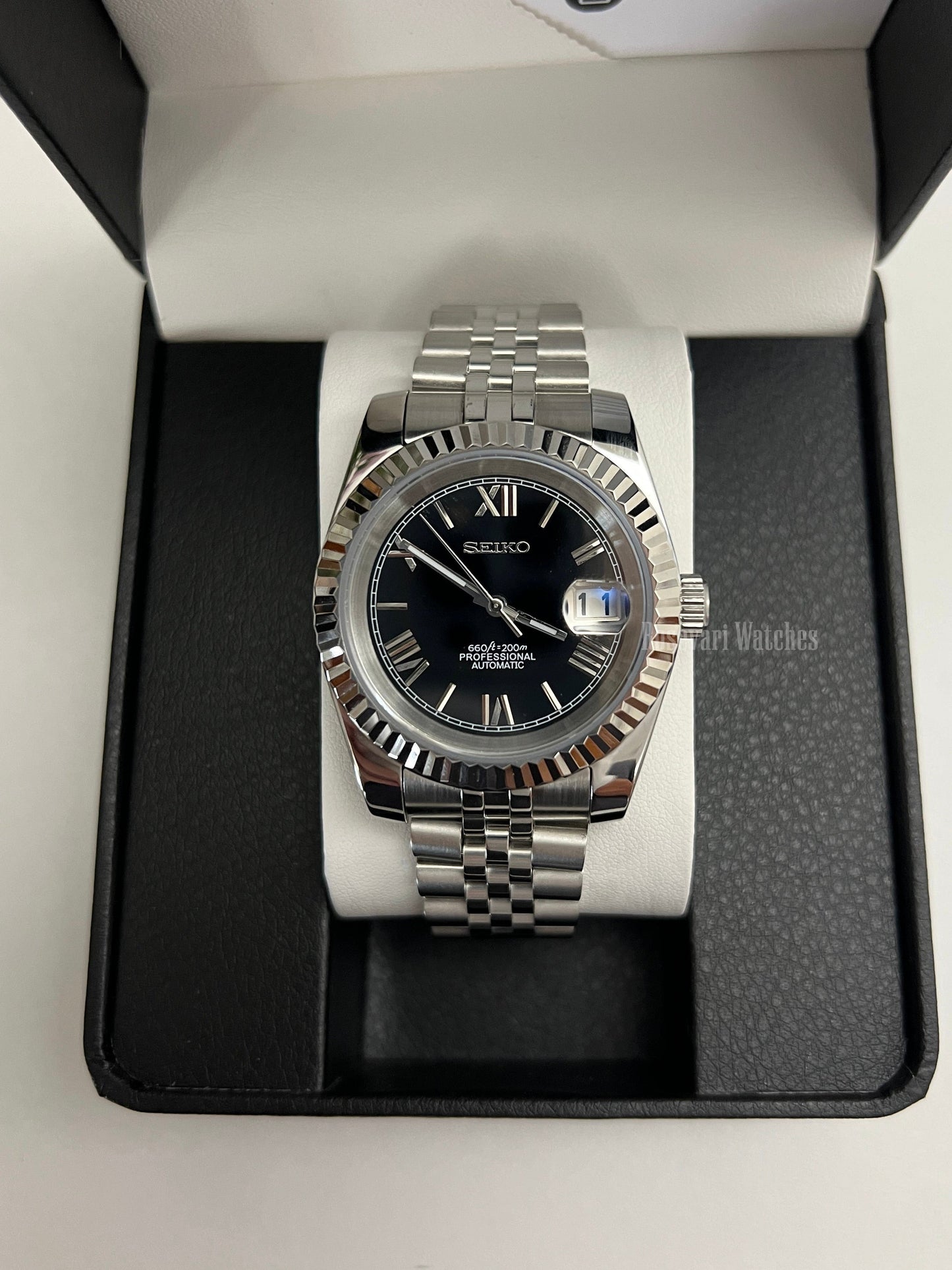 Datejust (Black Roman) Seiko NH35 automatic mod watch. A black dial watch with a silver fluted bezel and jubilee bracelet inside a box in a high angle shot.