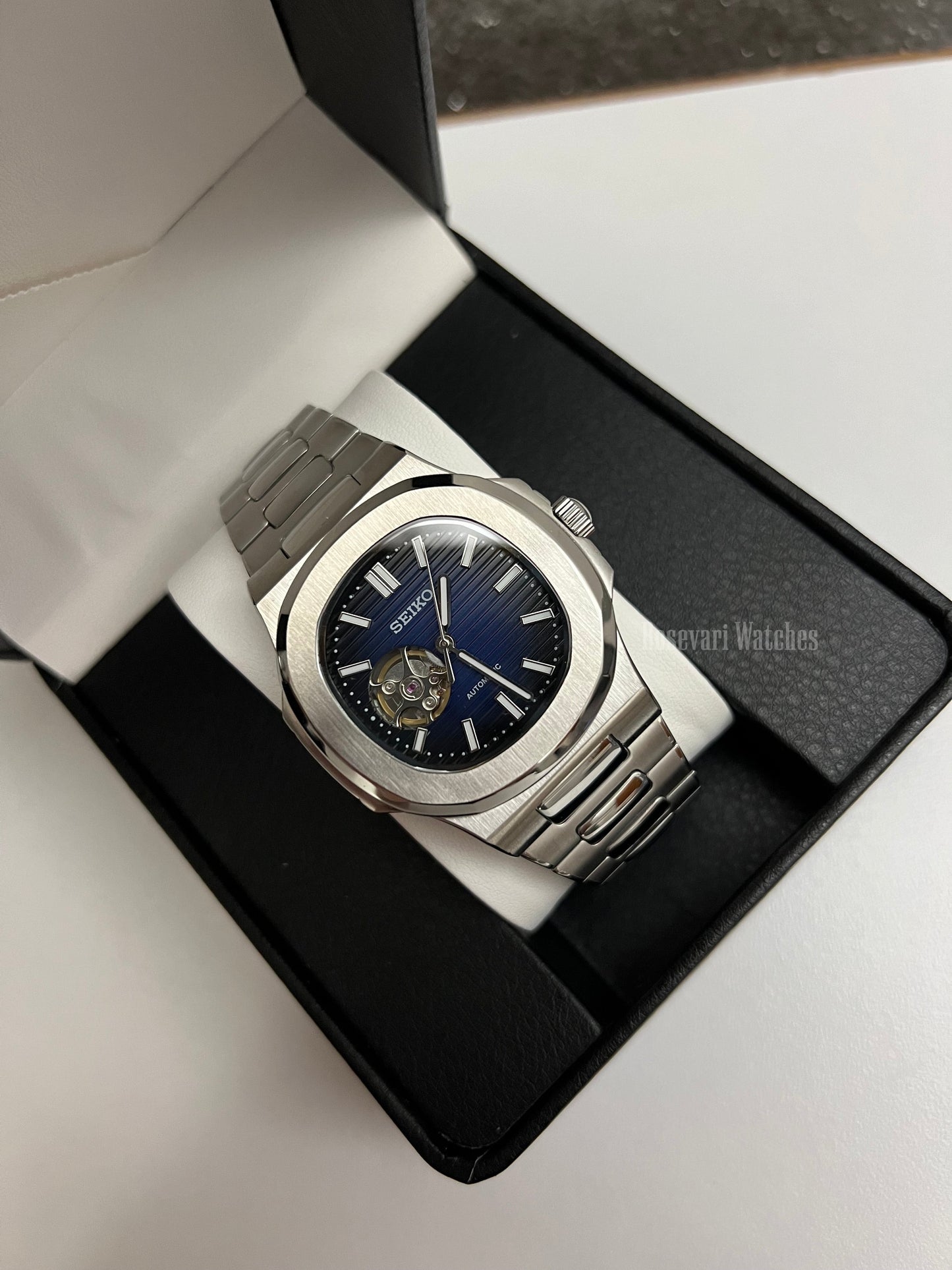 Nautilus (Open Heart, Royal Blue) Seiko NH38 open-heart automatic mod watch. A full watch shot in a box showing a blue dial and silver bezel with a metal link bracelet.