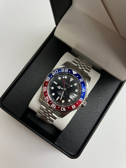 GMT (Pepsi) Seiko NH34 GMT automatic mod watch. A full watch shot inside a box shows a black dial with a blue and red bezel on a silver jubilee bracelet.
