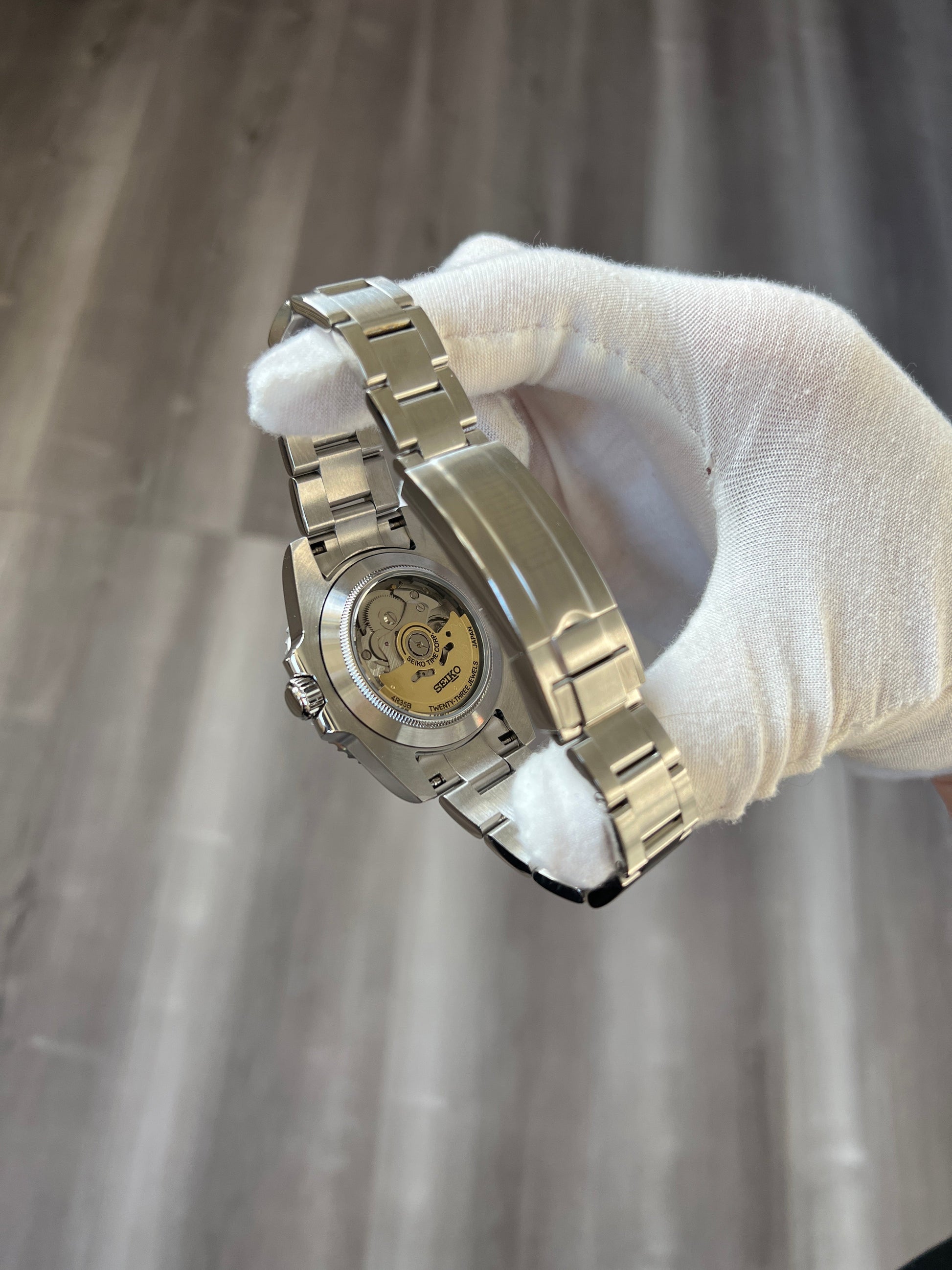 Submariner (Kermit) Seiko NH35 automatic mod watch. A close up view of the watch caseback showing the internal movement mechanism held by a gloved hand.